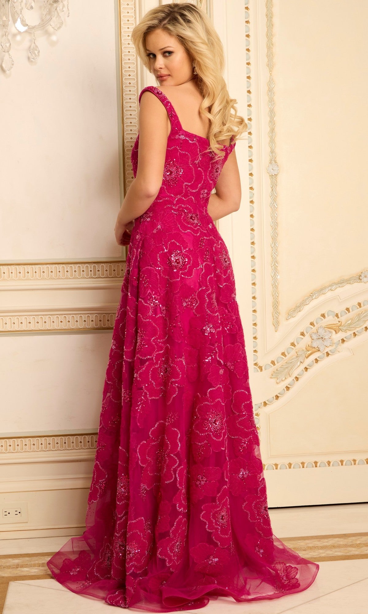 Wearing the Jovani 46471, a bright pink floor-length prom dress with a square neckline and beaded embellishments, a woman stands slightly turned away in an ornate room with cream walls and gold trim.